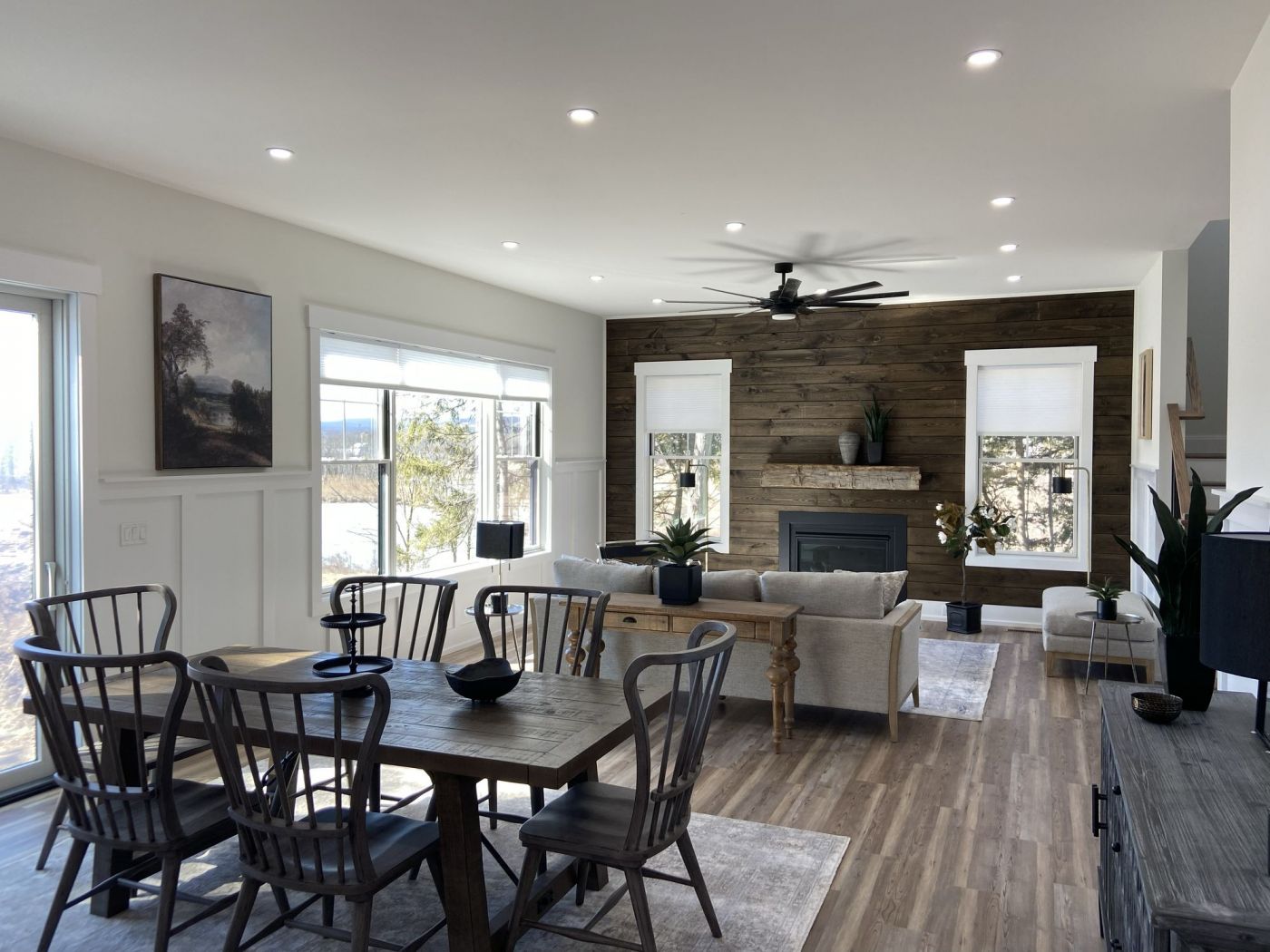 Modern living and dining area with wooden accents, large windows, and ceiling fan. Neutral tones and sleek furnishings.