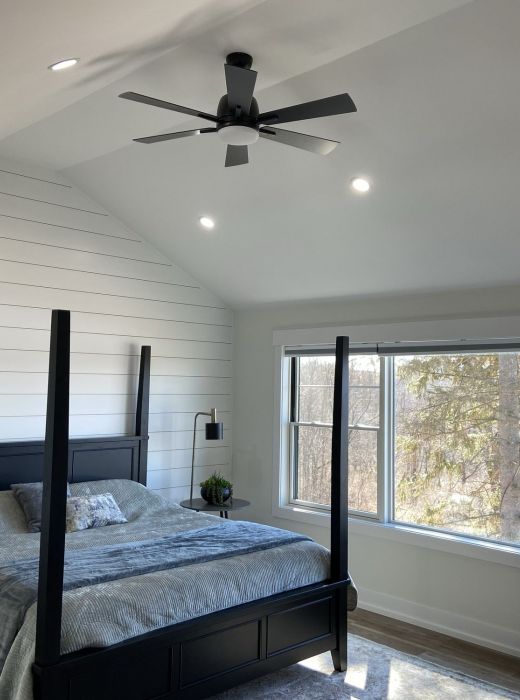 Modern bedroom with a dark four-poster bed, shiplap wall, large window, ceiling fan, and natural light at Mountain Crest Reserve