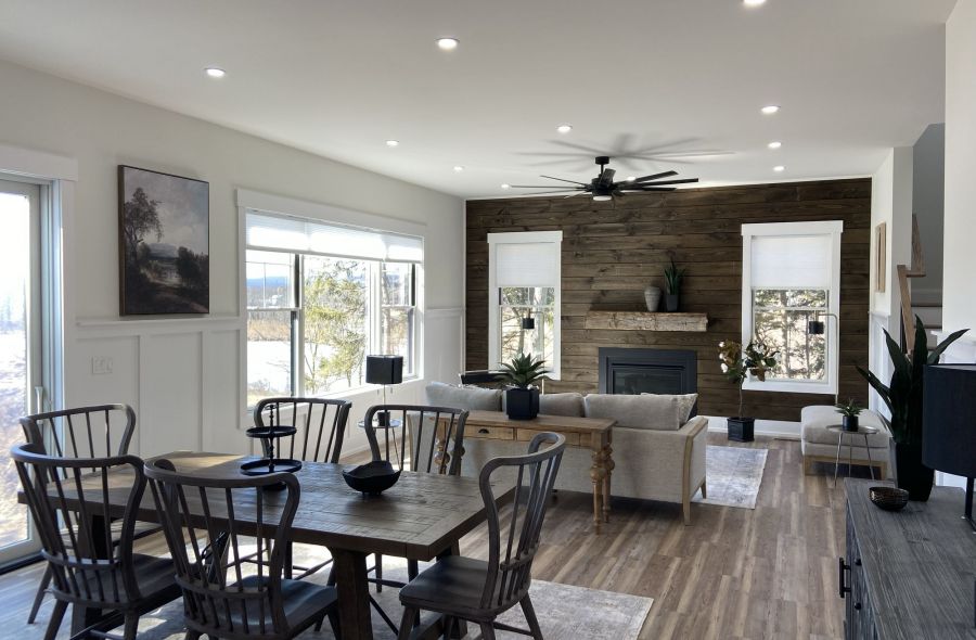 Modern open-concept living room and dining area with wooden floor, fireplace, and large windows.
