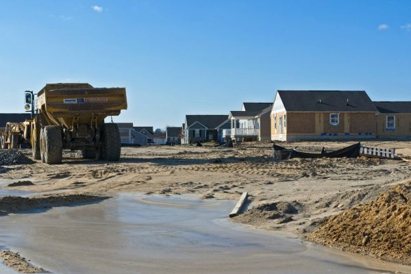 Construction site at Mountain Crest Reserve with several houses, a large dump truck, and a muddy area under a clear blue sky.