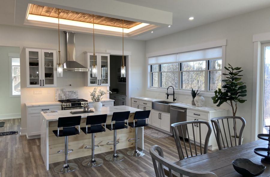 Modern kitchen with an island, barstools, pendant lights, stainless steel appliances, and large windows.