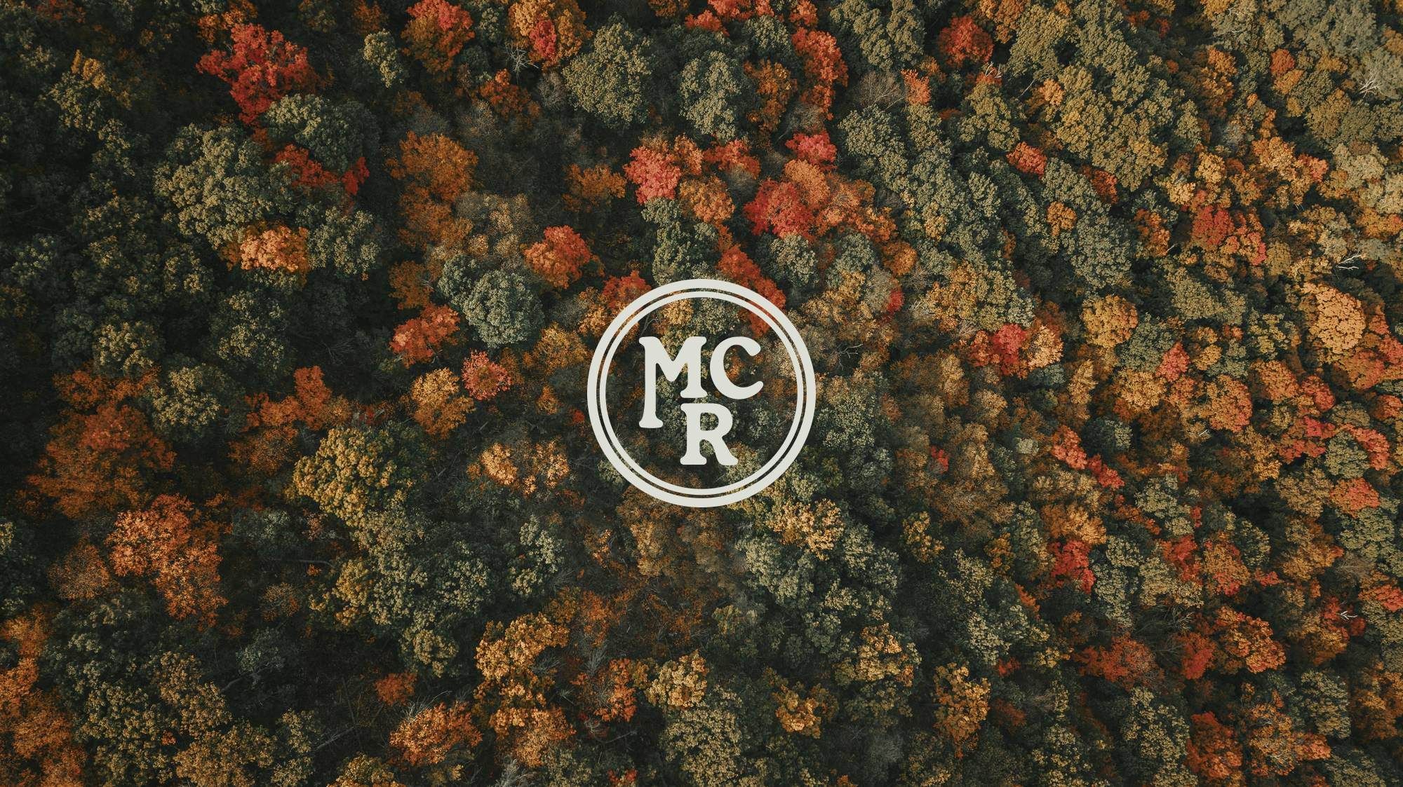 Aerial view of a colorful forest in autumn with an "MCR" logo in the center.