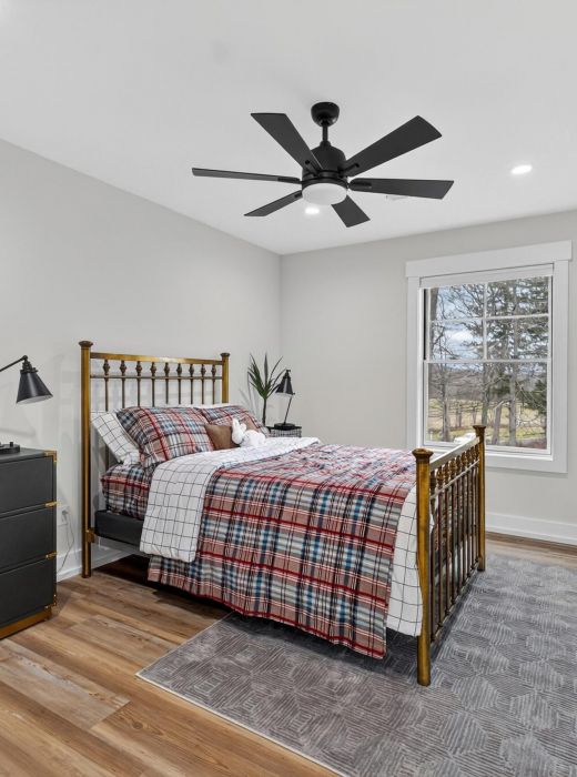 A cozy bedroom with a plaid bedspread, black dresser, plants, and a window letting in natural light.