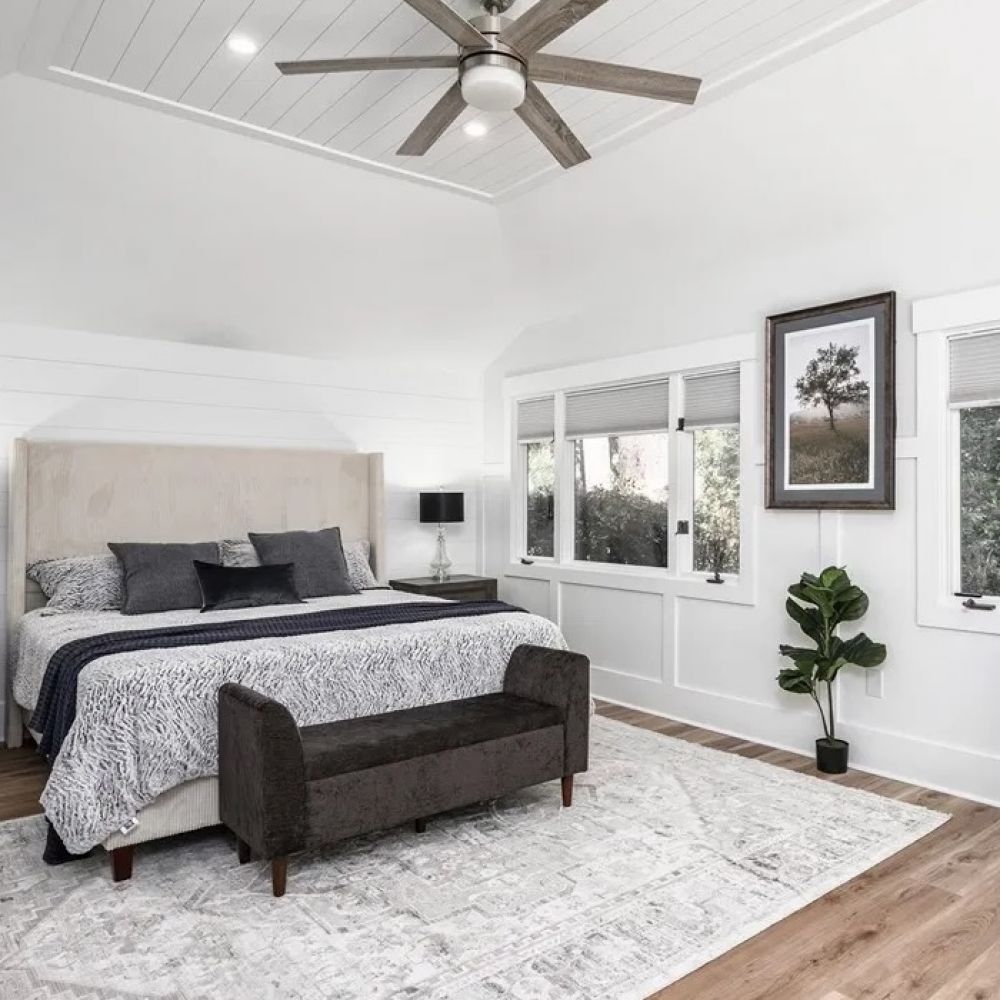 Spacious bedroom with a large bed, bench, armchair, ceiling fan, and large windows overlooking greenery at Mountain Crest Reserve.