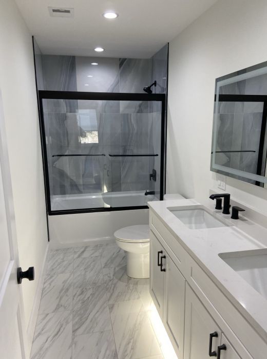 Modern bathroom with dual sinks, white cabinets, marble floor, and glass-enclosed bathtub with shower at Mountain Crest Reserve