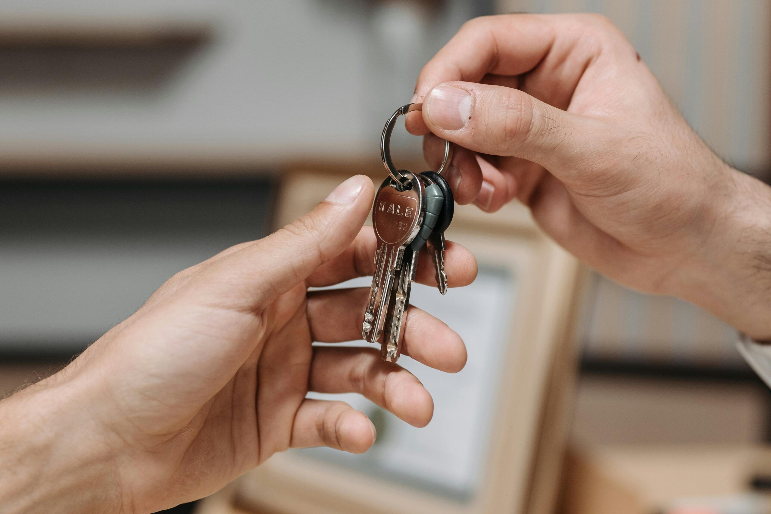 Hand holding house-shaped keychain over coins and a wooden box.