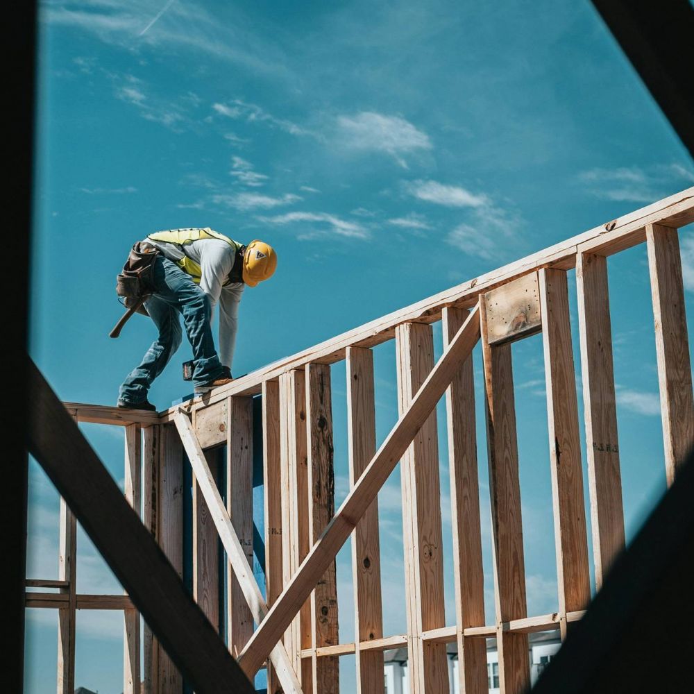 Construction worker in a yellow hard hat standing on a wooden frame under a clear blue sky at Mountain Crest Reserve.